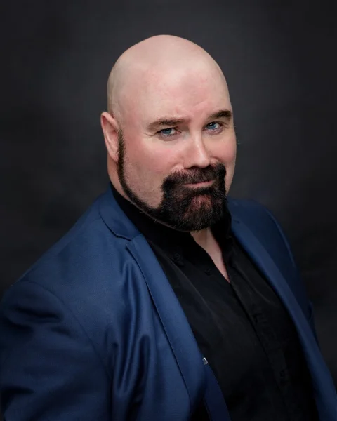Matt Whitfield Headshot - Matt Whitfield in a blue suit looking rakishly handsome with a lopsided grin