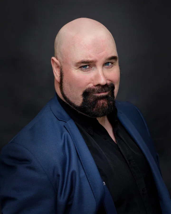 Matt Whitfield Headshot - Matt Whitfield in a blue suit looking rakishly handsome with a lopsided grin