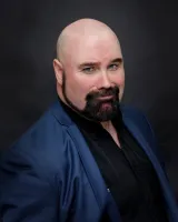 Matt Whitfield Headshot - Matt Whitfield in a blue suit looking rakishly handsome with a lopsided grin