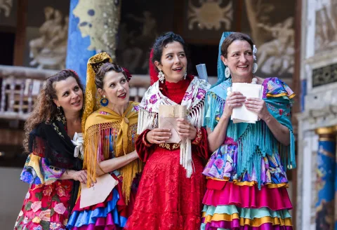 A group of four women dressed in colourful flamenco dresses and shawls and clutching pieces of paper.
