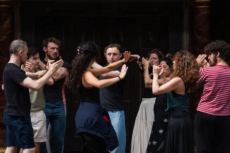 A group of people stand facing one another, each holding out their arms in front of them in various positions.