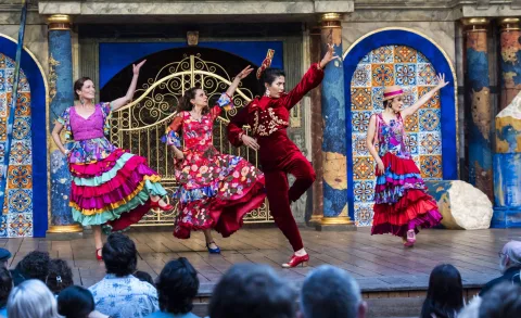Three women in flamenco outfits pose mid-dance, with one leg bent and one arm outstretched.