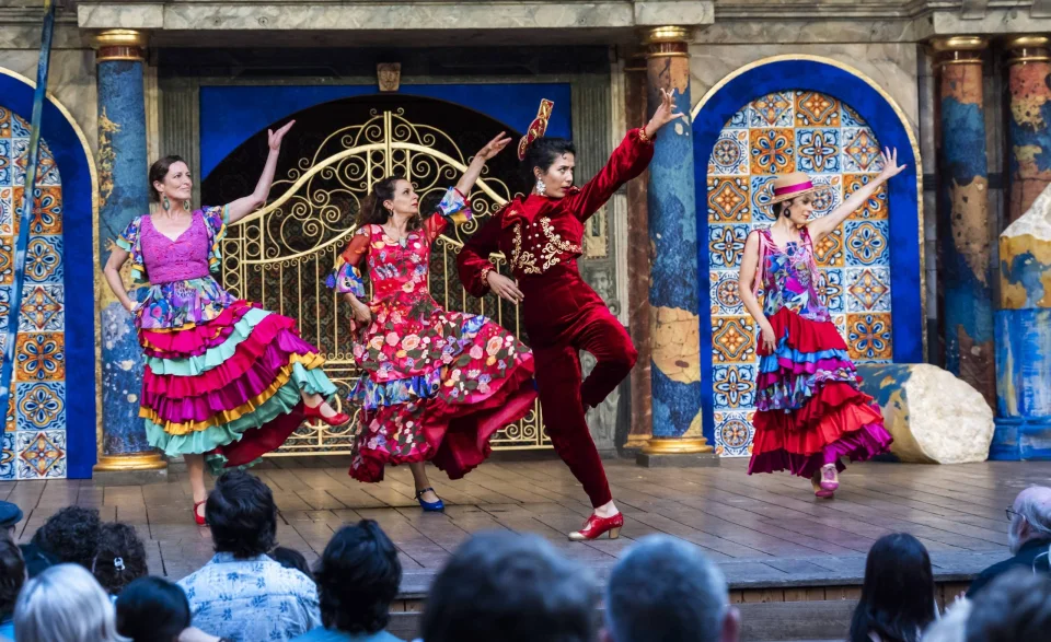 Three women in flamenco outfits pose mid-dance, with one leg bent and one arm outstretched.