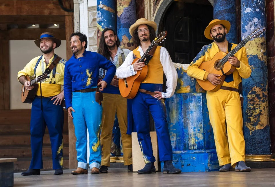 Five Spanish flamenco musicians dressed in blue and yellow. Two are holding guitars.