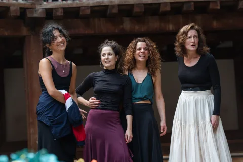 Four people stand beside each other. They each wear different long skirts and tops in purple, black, white and teal.