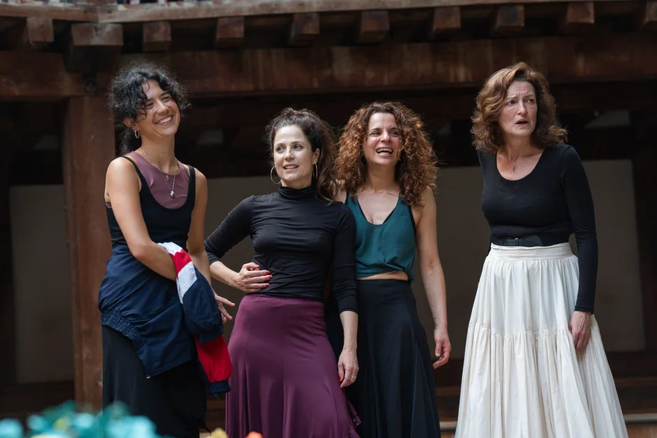 Four people stand beside each other. They each wear different long skirts and tops in purple, black, white and teal.