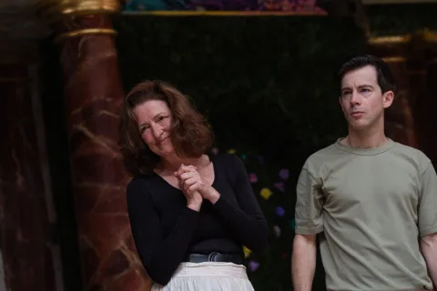 A white female with dark hair stands smiling with her hands clasped beside a white man wearing a green t-shirt.