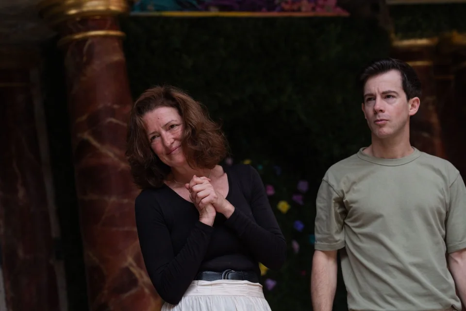 A white female with dark hair stands smiling with her hands clasped beside a white man wearing a green t-shirt.