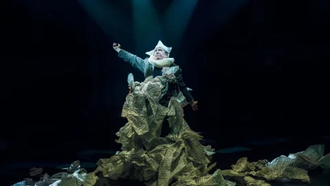 Phelim McDermott wrapped in lots of scrunched up sheet music, wearing a paper hat