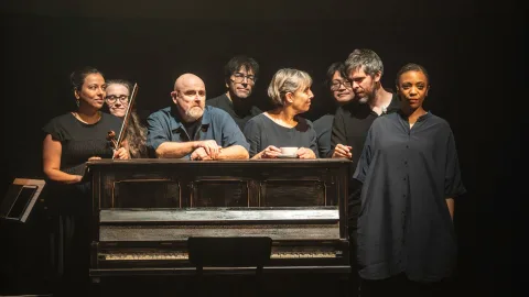 The company of Tao of Glass stand around an old piano