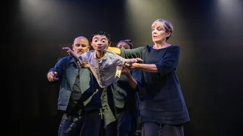 Three puppeteers move to make a small puppet of a boy fly through the air