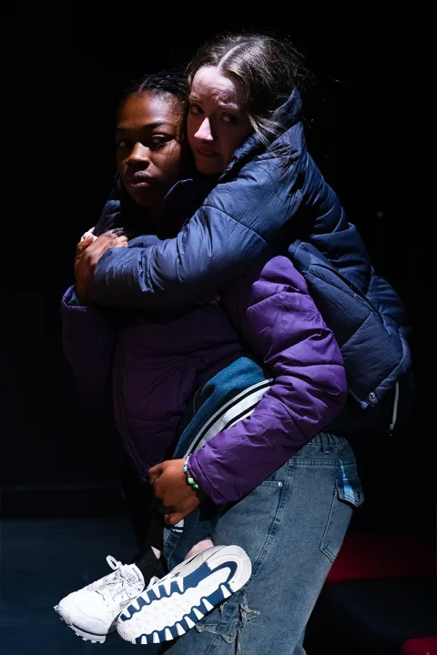 Katie (Kelise Gordon-Harrison) carries Tia (Mollie Milne) on her back.
