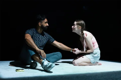 AJ (Taqi Nazeer) and Tia (Mollie Milne) sit together, she is grasping his hand and staring into his eyes pleadingly.