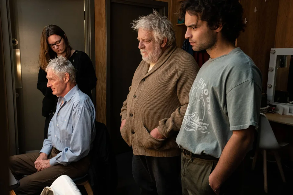 Sebastian De Souza, Simon Russell Beale and Michael Simkins getting ready backstage. They sit at dressing tables and stand in front of lit mirror.
