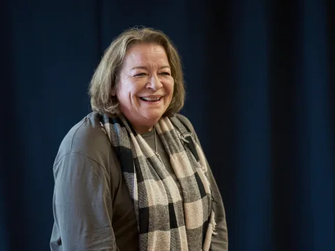 Clare Higgins is wearing a a large chequered scarf around her neck and is mid laughter.