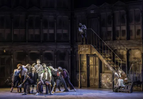 Nick Piazza (Joe Boyle)  singing surrounded by ensemble while Serena sits on the stairs. Credit: Johan Persson