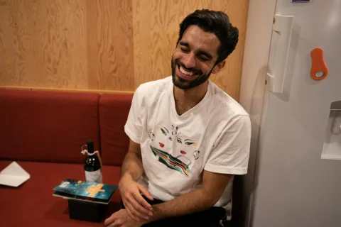 A man (Eben Figueiredo) is sat on a sofa with his eyes closed laughing