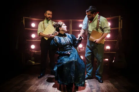 A woman sits in a chair and is interrogated by two police officers.