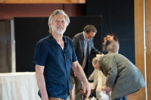 A man wearing a dark blue shirt stands in the centre of the image smiling.