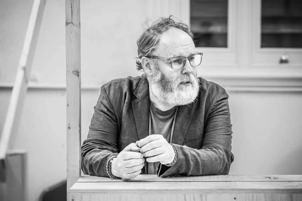 David Ganly leans against a surface with his hands together. He looks over his left shoulder.