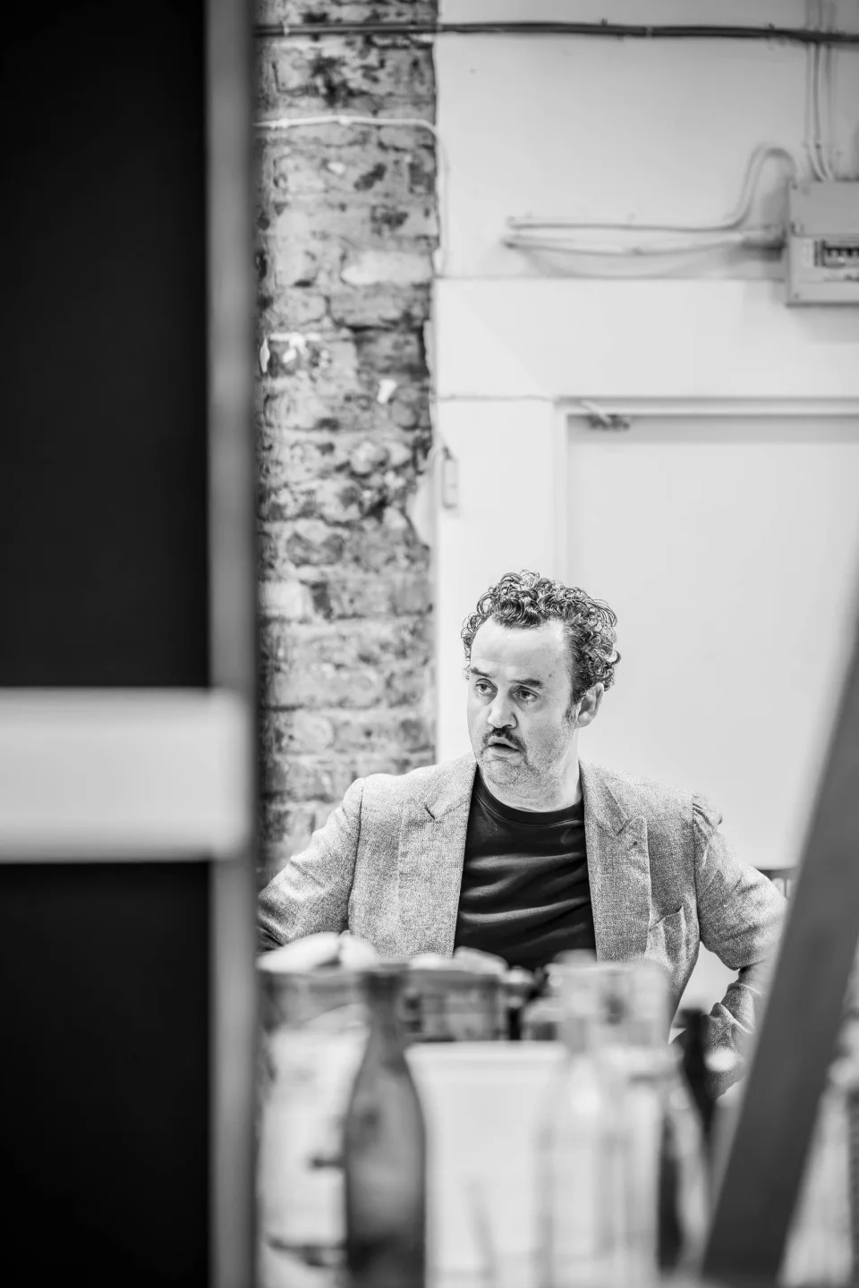 Daniel Mays stands with his hands on his hips. He is looking over to the right with a shocked expression on his face.