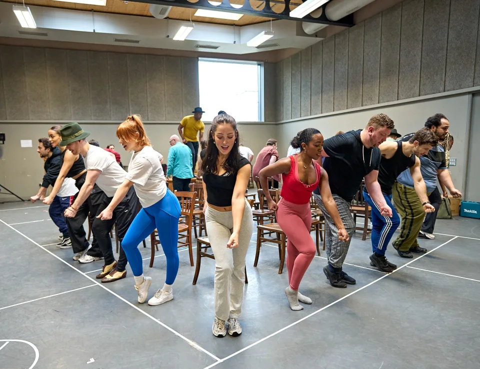 Stood in an arrow with one person at the point the cast of Guys & Dolls dance in unison.